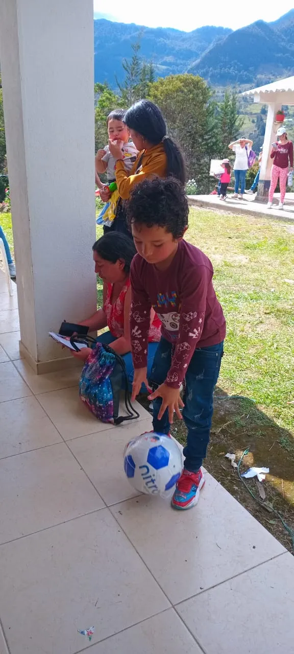 Niños jugando con un balón junto a su mamá durante una jornada de entrega de regalos de la Fundación Dejando Huellas en Ubalá, Cundinamarca